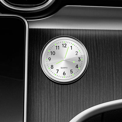 Car dashboard clock with silver frame and white face on a black car interior.