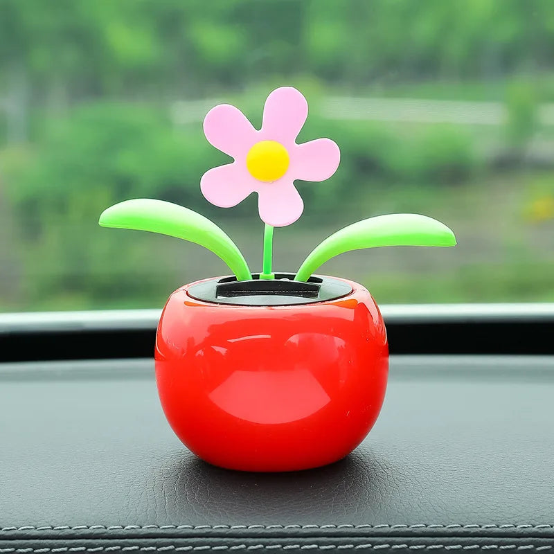 Colorful toy flower in a red pot on a car dashboard with a blurred green outdoor background