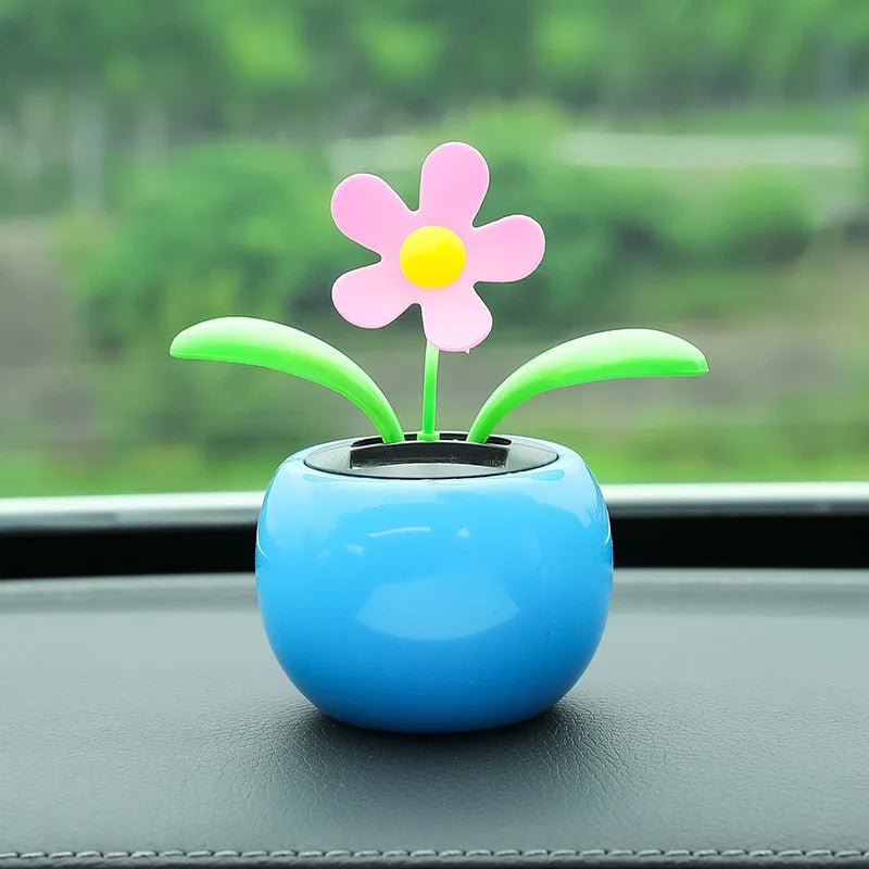 Decorative flower on a blue base on a car dashboard with a blurred green outdoor background