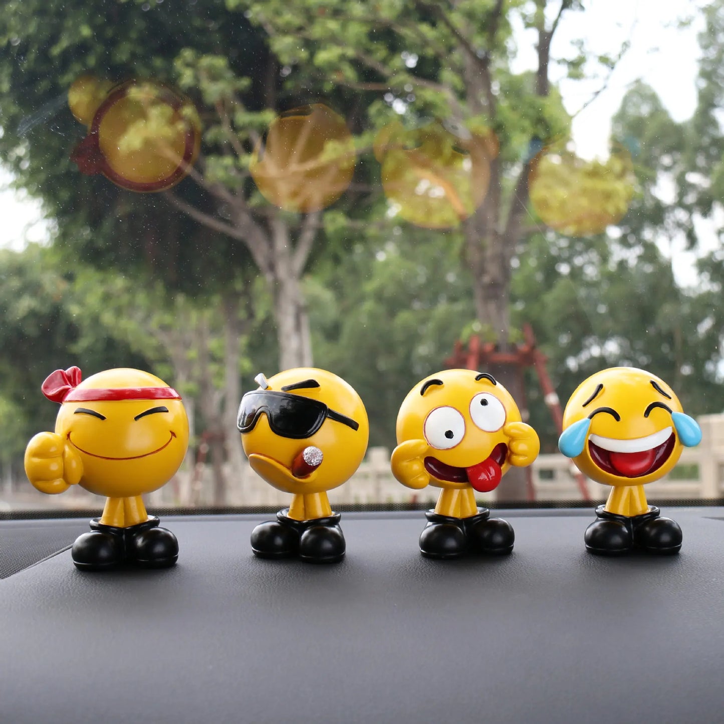 Four emoji figurines on a car dashboard with a blurred outdoor background