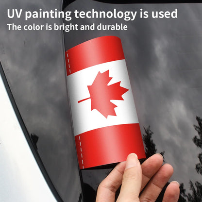 Hand holding a car window decal with a red and white design, likely a flag, against a dark background.