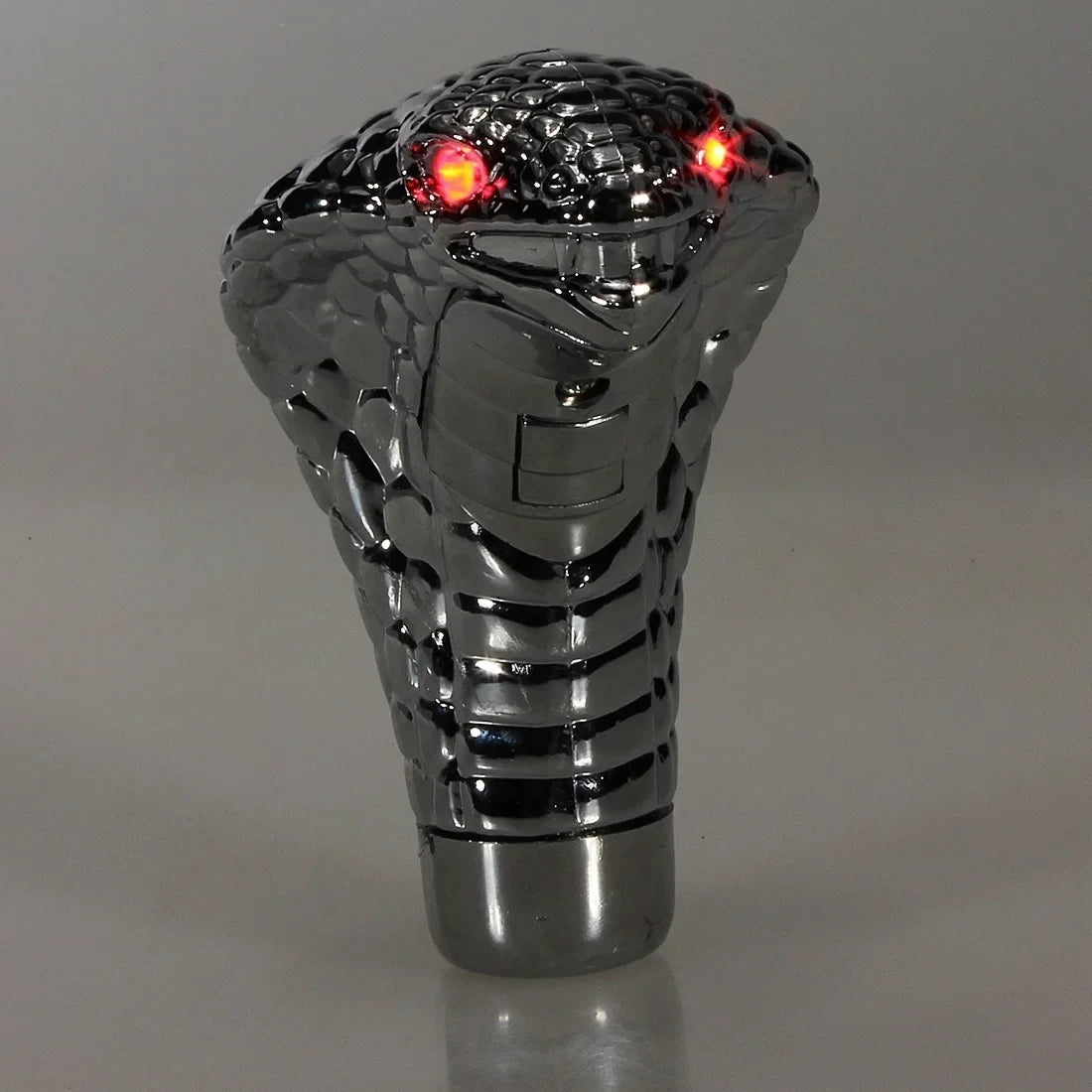 Metallic gear shift knob with snake design and red lights on a gray background