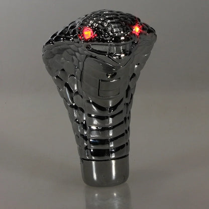 Metallic gear shift knob with snake design and red lights on a gray background