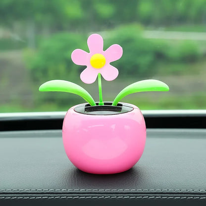 Pink flower-shaped toy on a car dashboard with a blurred green outdoor background