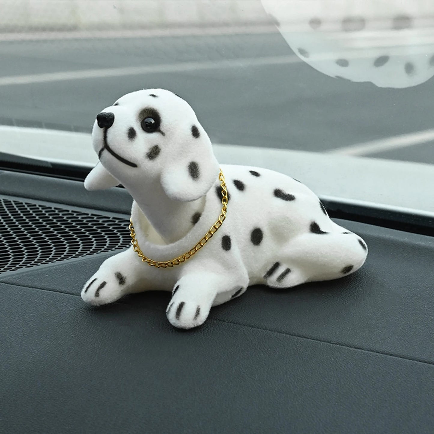 Plush dalmatian dog toy with a gold chain on a car dashboard.