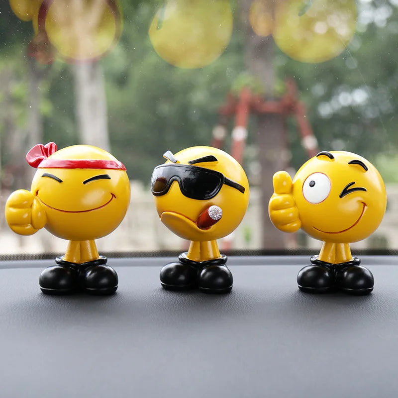 Three yellow emoji figurines with different expressions on a car dashboard.