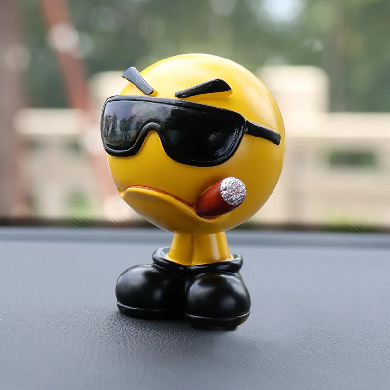 Yellow emoji figurine with sunglasses and a blingy lip on a car dashboard.